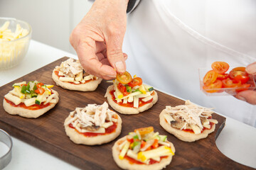 Adding toppings to the mini pizzas. Delicious homemade mini pizzas preparation.