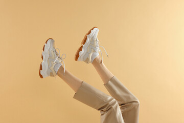 Woman wearing pair of new stylish sneakers on beige background, closeup