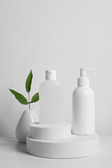 Bottles of cosmetic products and leaves on white wooden table