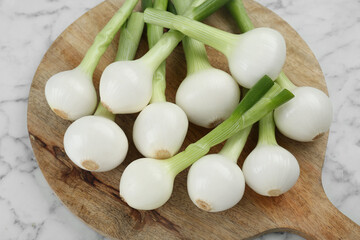 Wooden board with green spring onions on white marble table, closeup