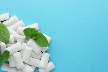 Pile of tasty white chewing gums and mint leaves on light blue background, top view. Space for text © New Africa