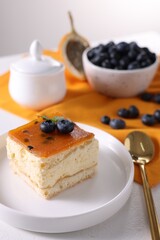 Piece of delicious cheesecake with blueberries and spoon on white table, closeup. Space for text