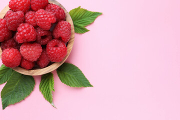 Tasty ripe raspberries and green leaves on pink background, above view. Space for text