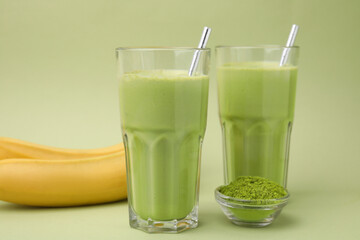 Glasses of tasty matcha smoothie and powder on pale green background