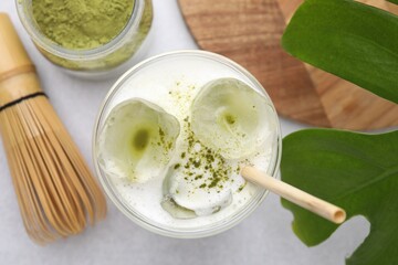 Glass of tasty iced matcha latte, leaf, powder and bamboo whisk on white table