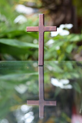 cross representing God in Christianity is placed on mirror and its reflection can be seen on blurred background of nature. cross on background is blurred and there is Copy Space on side for text.