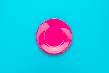 Top view photo of empty fashion fuchsia colored plate. Minimalist flat lay image of ceramic plate over turquoise blue background with copy space and central composition.