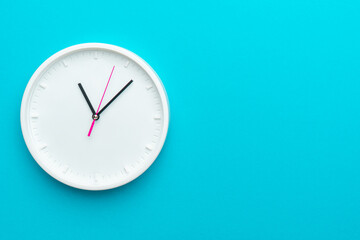 White wall clock with yellow second hand hanging on wall. Close up image of plastic wall clock over turquoise blue background with copy space. Photo of time management or time is going concept