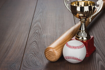 Golden trophy cup and baseball bat and ball on the wooden table