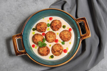 fishballs in white sauce with drops of mint oil and sriracha on a grey steel plate with a grey tablecloth