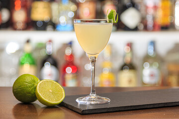 light beige cocktail on the bar against the background of blurred bottles in the bar
