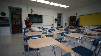 Happy teacher entering an empty classroom, turning lights, on optimistic about the future of education. US American flag and smart board in room.