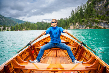 Man sitting in big brown boat at Lago di Braies lake in cloudy day, Italy. Summer vacation in Europe