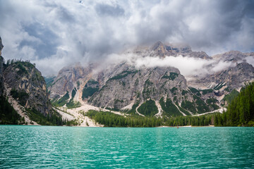 Braies lake surrounded by pine forests and the rocky ranges of the Dolomites in cloudy day, Italy.