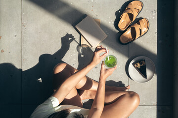 Summer composition with slippers, books, cake and lemonade in female hands.