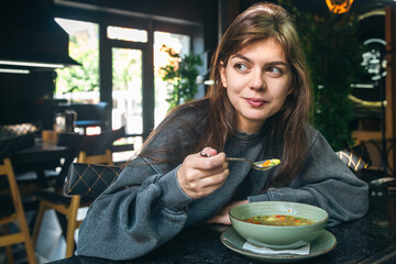 Attractive woman is eating vegetable soup in a cafe.