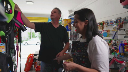 Person shopping at local Pet Store. Female employee wearing apron helping man to buy leash for Dog