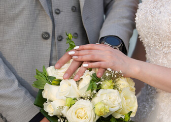 Obraz na płótnie Canvas Hands of newlyweds with wedding rings on a bouquet of roses