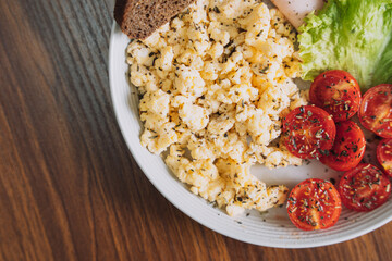 Sliced vegetables with scrambled eggs on a white plate on a wooden table.