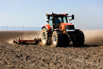 Fototapeta premium Tractor preparing land for sowing. Tractor with cultivator handles field before planting. Preparing land for sowing at spring, .