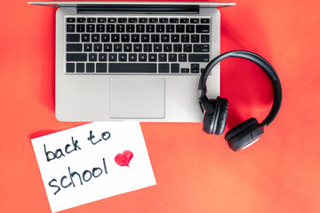 Laptop and headphones on red background, back to school concept.
