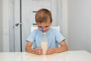 Child drinks delicious chocolate milk at home. Cute little boy drinks glass of milk and blows milk bubbles while sitting at table