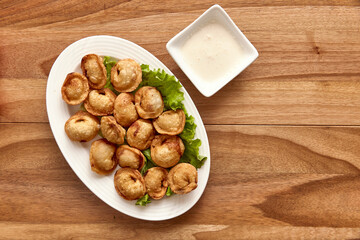 White plate with fried dumplings on lettuce on the wooden table with sour cream near it. Top view, flat lay