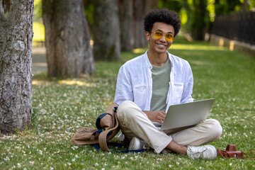 Obraz premium Man in light clothes sitting on the grass and working on laptop