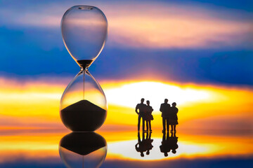 miniature people. silhouettes of different people watching the sunset next to the hourglass. end of life.