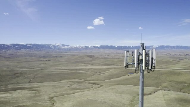 Cinematic drone shot flying backwards to reveal the 4G/5G antenna array at the top of a cell phone tower mast over a rural landscape (Aerial 4K HDR ProRes)
