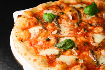 Selective focus on traditional Neapolitan pizza with anchovy, capers, mozarella cheese, garlic chips and fresh basil leaves.