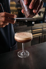 Fototapeta na wymiar Barista decorating martini cocktail with grated chocolate in bar