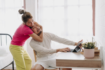 Asian wife pulling husband out of the desk to stop working. Funny couple fight.