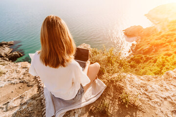 Freelance woman working on a laptop by the sea, typing away on the keyboard while enjoying the beautiful view, highlighting the idea of remote work.