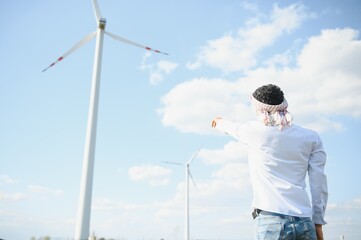 Engineer India man working at windmill farm Generating electricity clean energy. Wind turbine farm generator by alternative green energy. Asian engineer checking control electric power