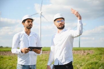 Two engineers discussing against turbines on wind turbine farm.