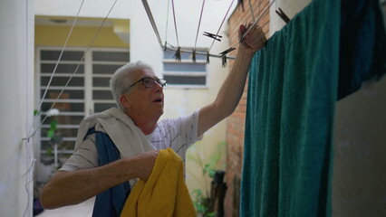 Older man removing towels from drying hangers in home backyard, elderly person doing household chore activities, casual domestic lifestyle scene in old age