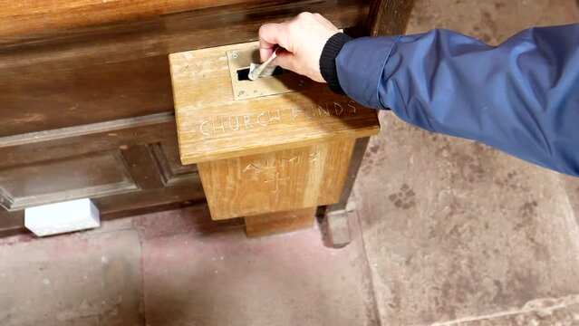 Helping church, donation. Hand putting 10 GB pound banknote into charity box close up.