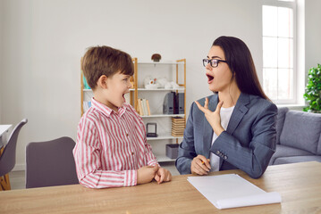 Professional young woman speech therapist training with a little boy patient at her office,...