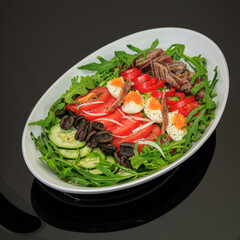 nicoise salad layered in a deep plate on a pure black table