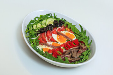 nicoise salad layered in a deep plate on a pure white table