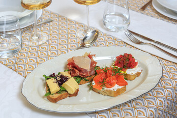 set of four bruschettas (camembert, tomatoes, salmon, jamon) served with a knife and fork with a glass of water and wine