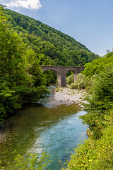Fototapeta na wymiar A view along the Baca river towards a stone arch railway bridge near the village of Klavze in Slovenia in summertime