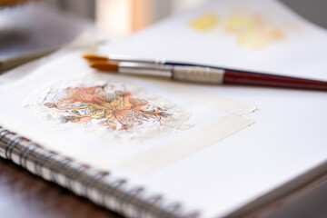 dos pinceles encima de bloc de dibujo pintado con acuarela a la luz de la ventana