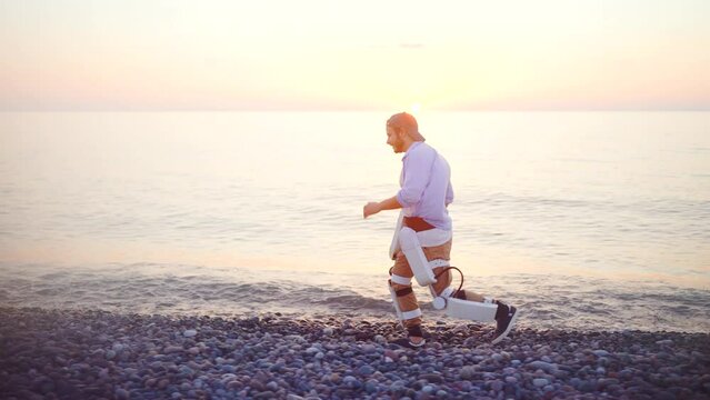 a happy man in an exoskeleton suit runs along the beach at sunset