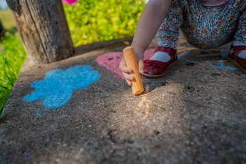 Child toddler girl with small red shoes drawing with chalk on countryside porch during summer evening