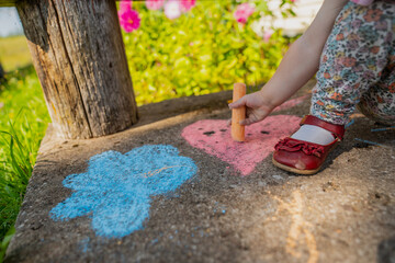 Little girl with red shoes drawing with orange chalk on a porch in countryside