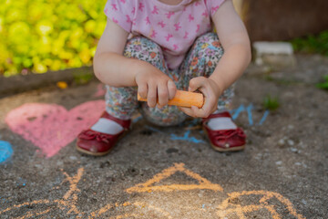 Small girl in red shoes playing and drawing with orange chalk in hands in summer on a porch