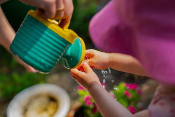 Small girl washing her hands with green children watering can