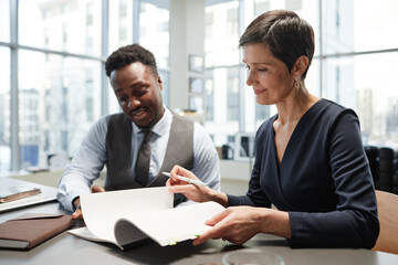 Portrait of elegant mature businesswoman signing documents with colleague in luxury office